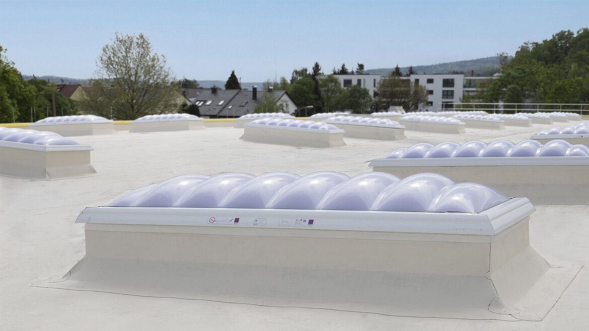 Several skylights on a white flat roof, with a residential area in the background
