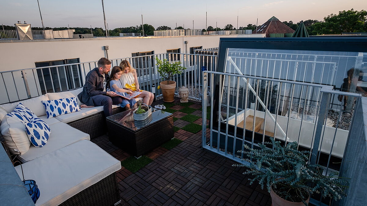 Family sitting on the roof terrace of their townhouse in Berlin with a flat roof exit at sunset.