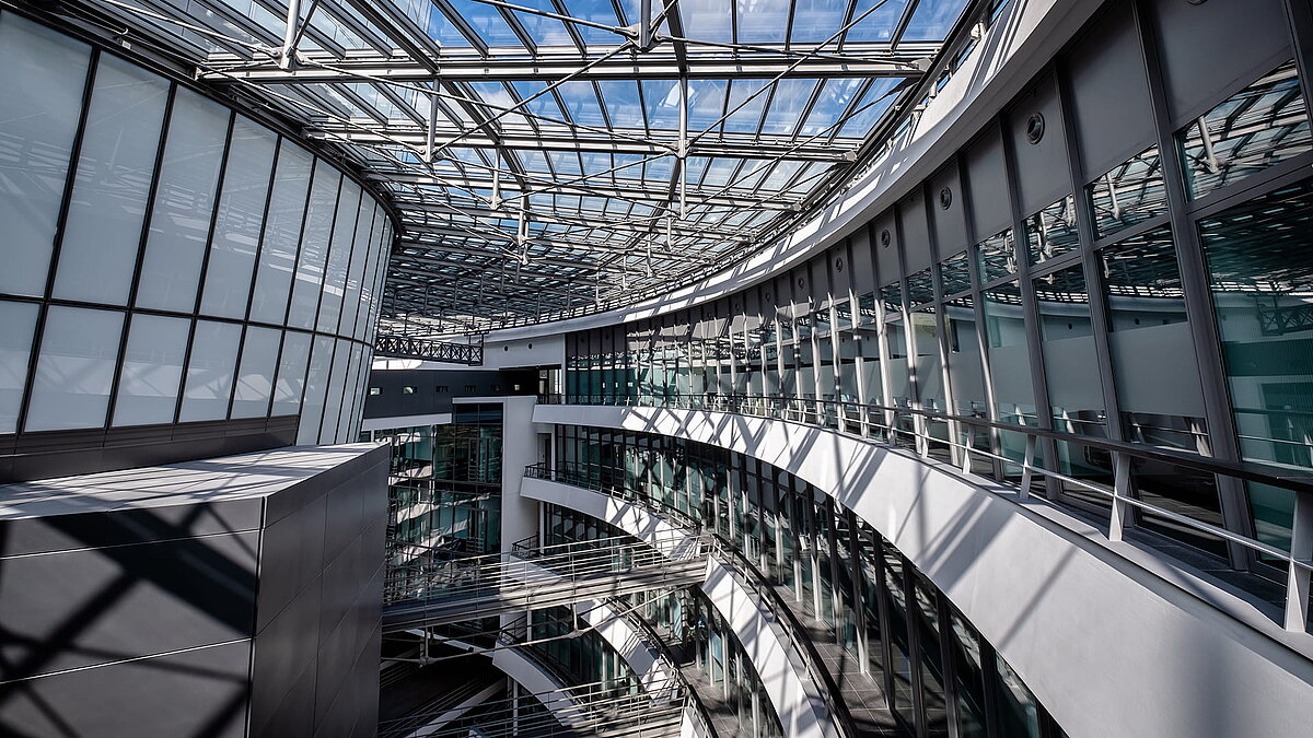 Interior view of the BMW Group Research and Innovation Centre (FIZ) featuring curved glass facades and an expansive glass roof channeling natural light into the modern office spaces.