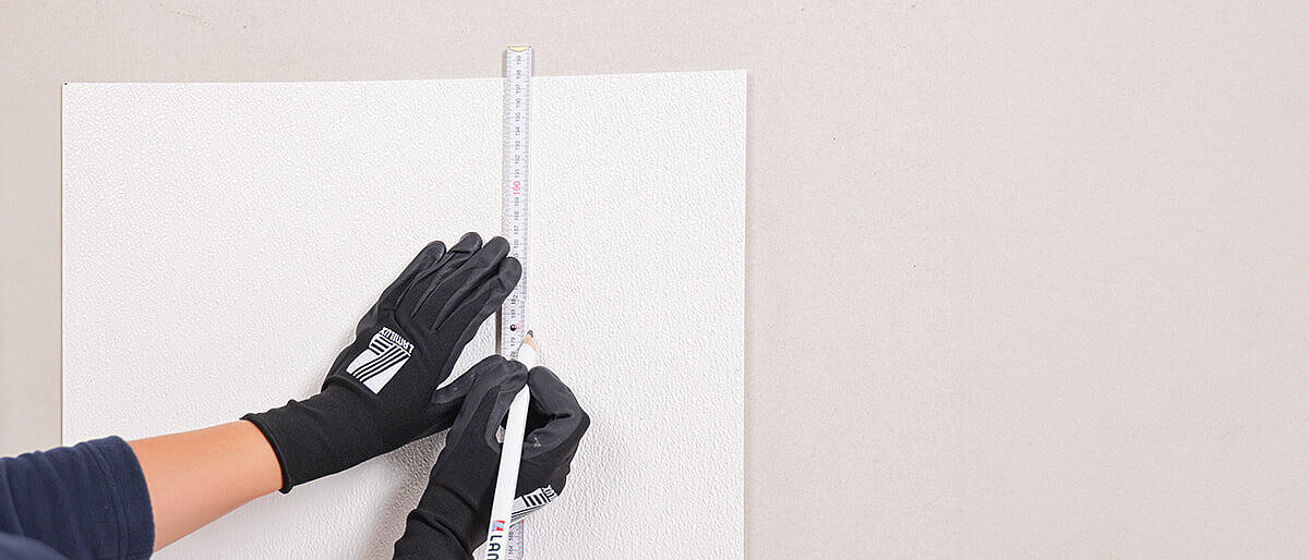 Person with gloves marking a white surface with a ruler and pencil