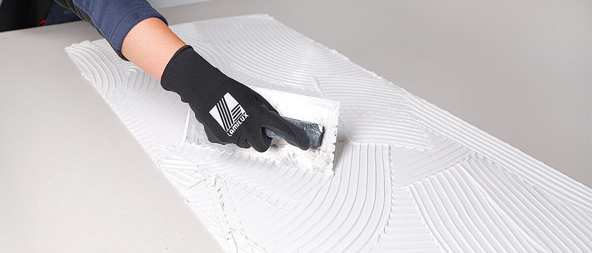 Person applying adhesive to a white surface with a trowel