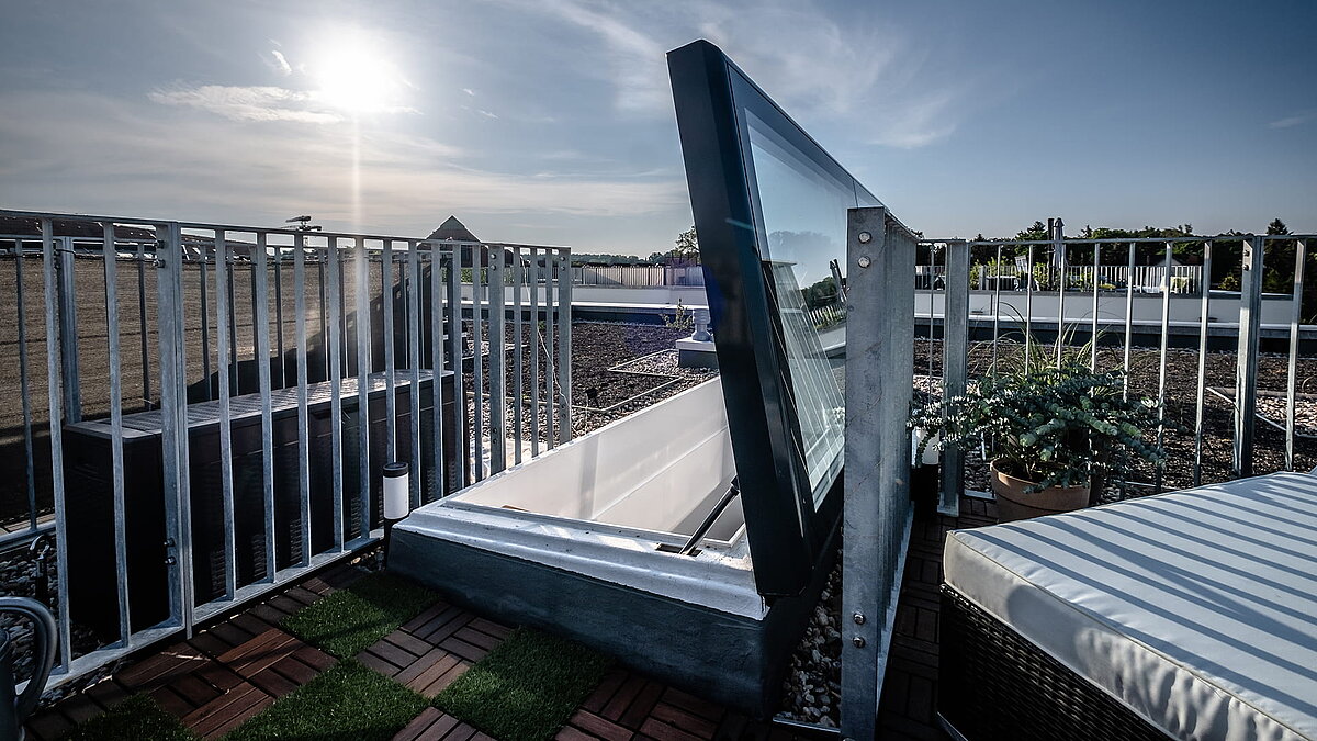 Flat roof exit at a townhouse in Berlin with modern glass cover and railing, sunlight in the background.