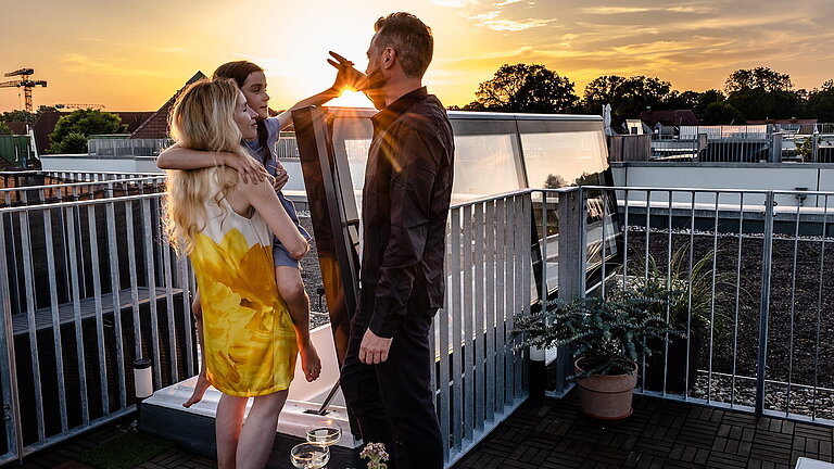 Family on the rooftop terrace of a townhouse in Berlin at sunset, next to a flat roof exit with a glass cover.