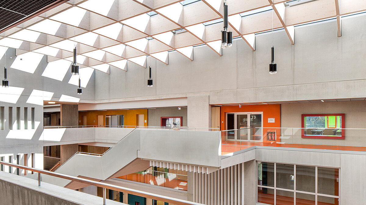 Interior of Willibald-Gluck-Gymnasium in Neumarkt with LAMILUX glass roof, modern concrete architecture, and colorful accents.
