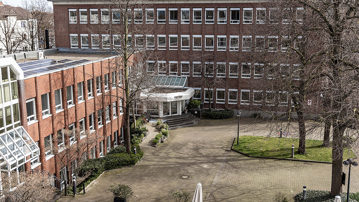 Exterior view of Factory Campus Düsseldorf with red brick building, glass roof, and courtyard.