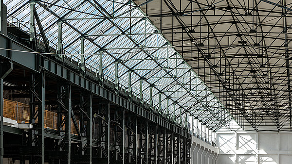 Interior view of Factory Campus Düsseldorf featuring glass roof, steel beam structure, and industrial charm.