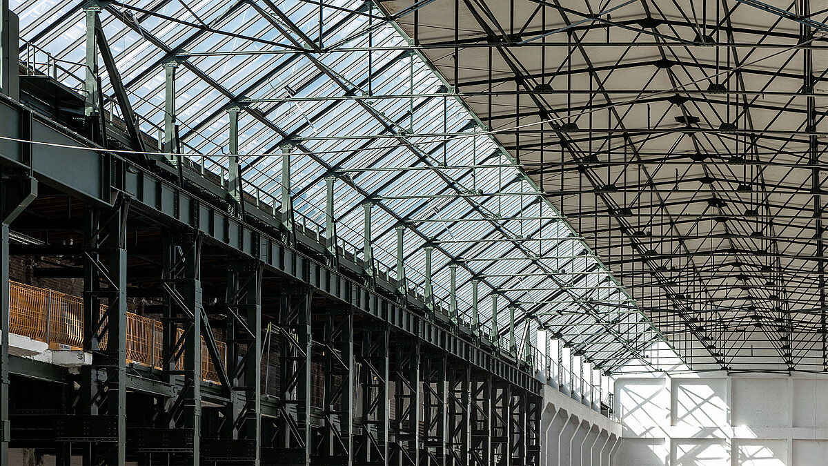 Interior view of Factory Campus Düsseldorf featuring glass roof, steel beam structure, and industrial charm.