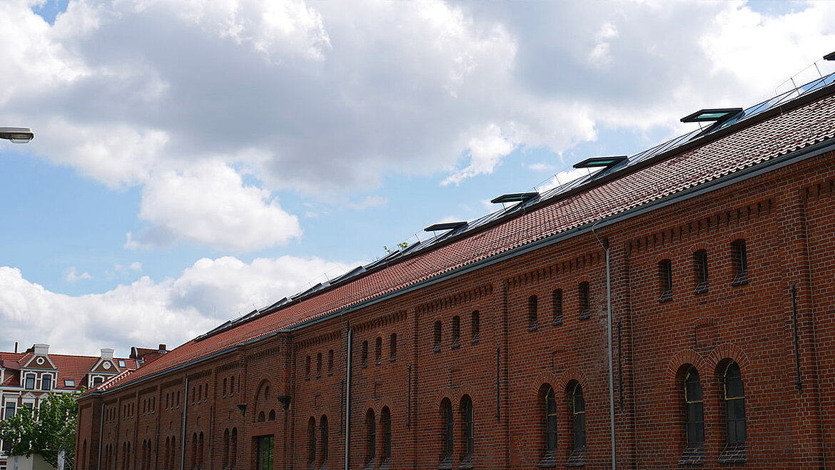 Tiled roof of a historic industrial hall with skylights under a blue sky.