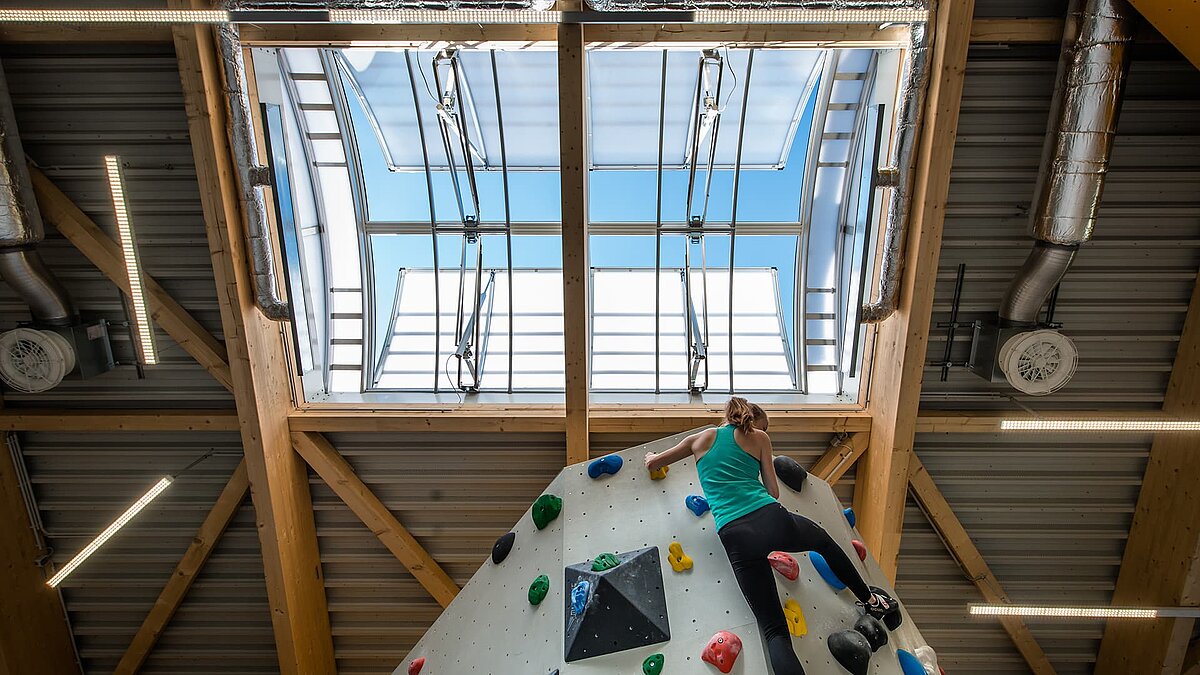 OWL climbing center with a climbing wall and an open skylight allowing daylight into the hall. A woman is climbing the colorful wall.