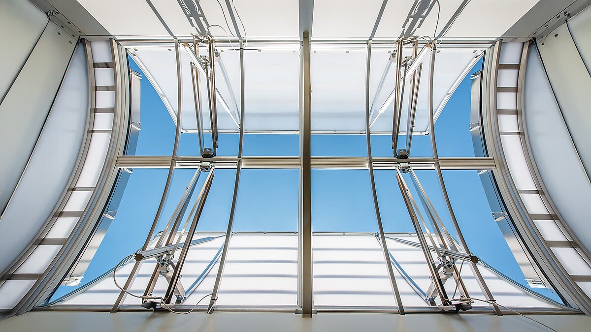 Close-up view of a large, curved glass roof with metal frames and ventilation elements at the OWL climbing center.