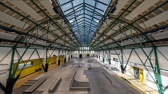 Historic industrial hall with steel beams and large glass roof.