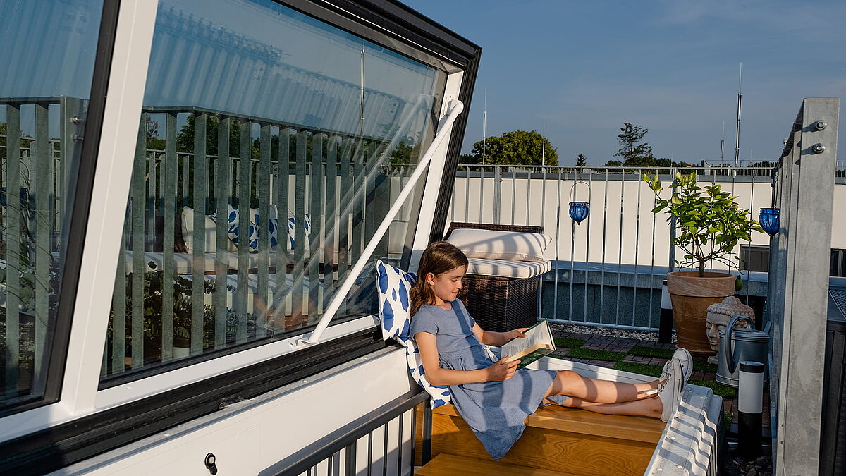 Girl reading a book on the rooftop terrace of a townhouse in Berlin, next to an open flat roof access.