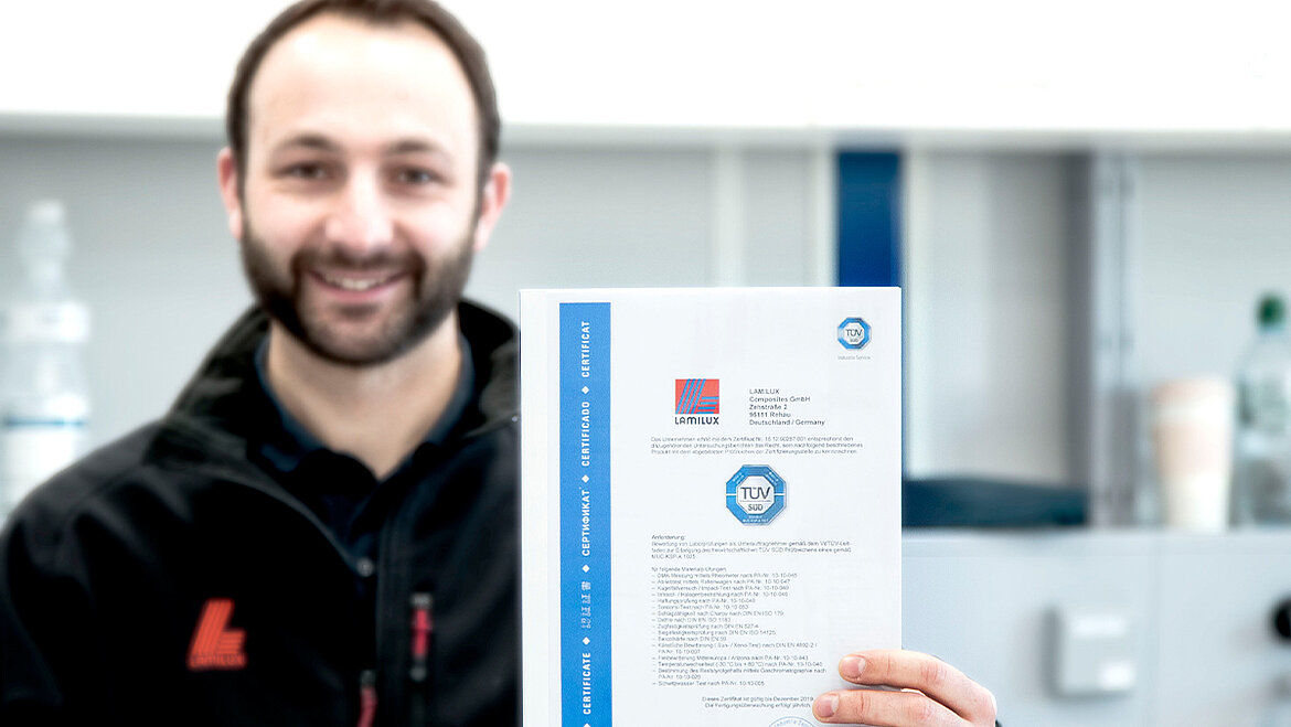 LAMILUX Composites has its test methods certified by TÜV Süd. Man laughing and holding certificate into the camera | insights by LAMILUX