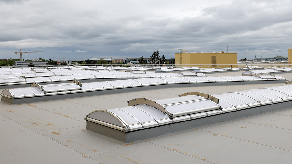 Large flat roof with many new roof skylights and a yellow building in the background.
