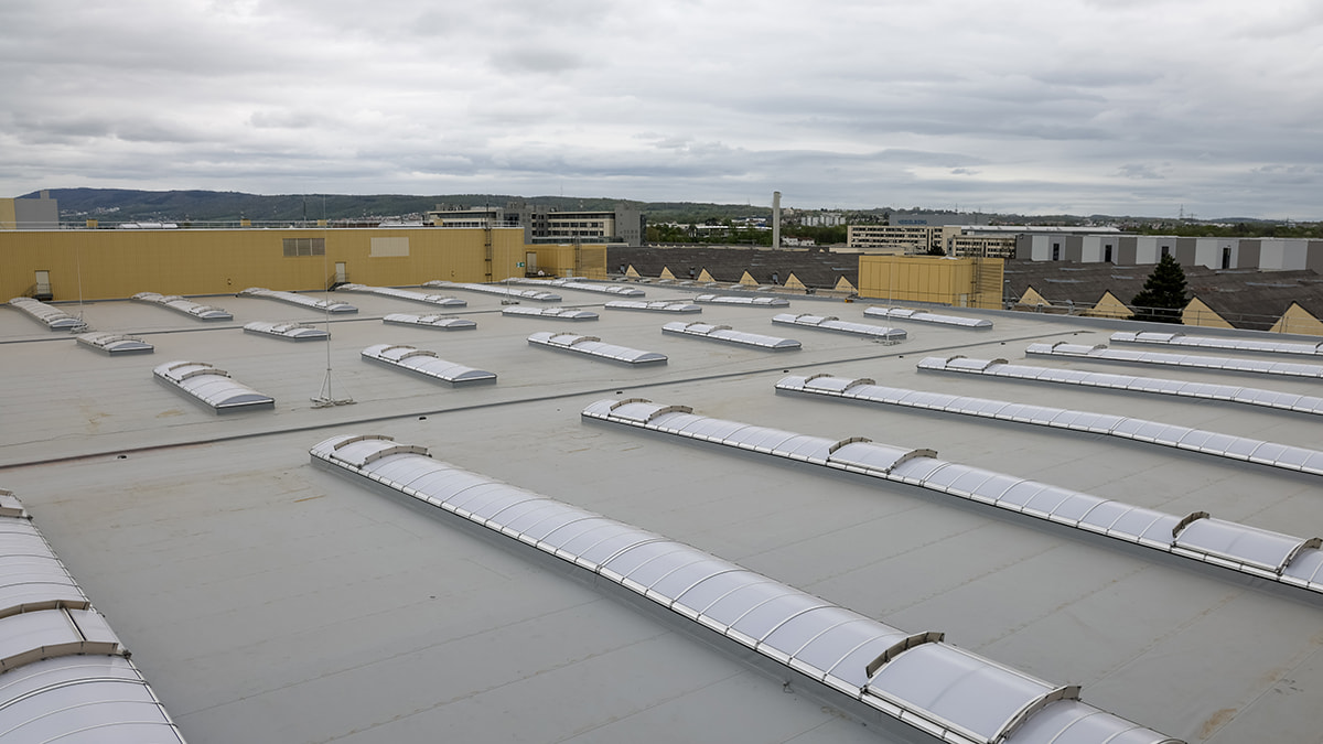 Panoramic view of a flat roof with many new roof skylights and surrounding city in the background.