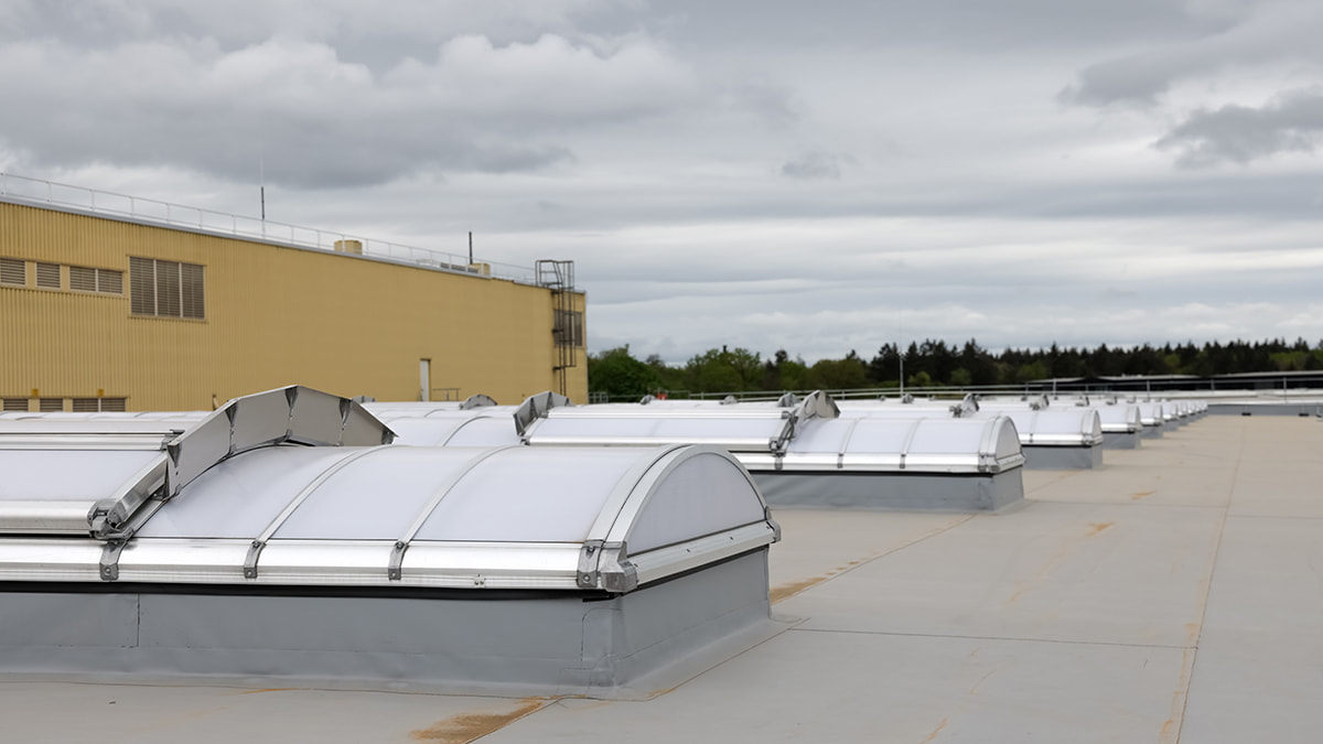 Multiple new roof skylights on a large flat roof with a cloudy sky in the background.