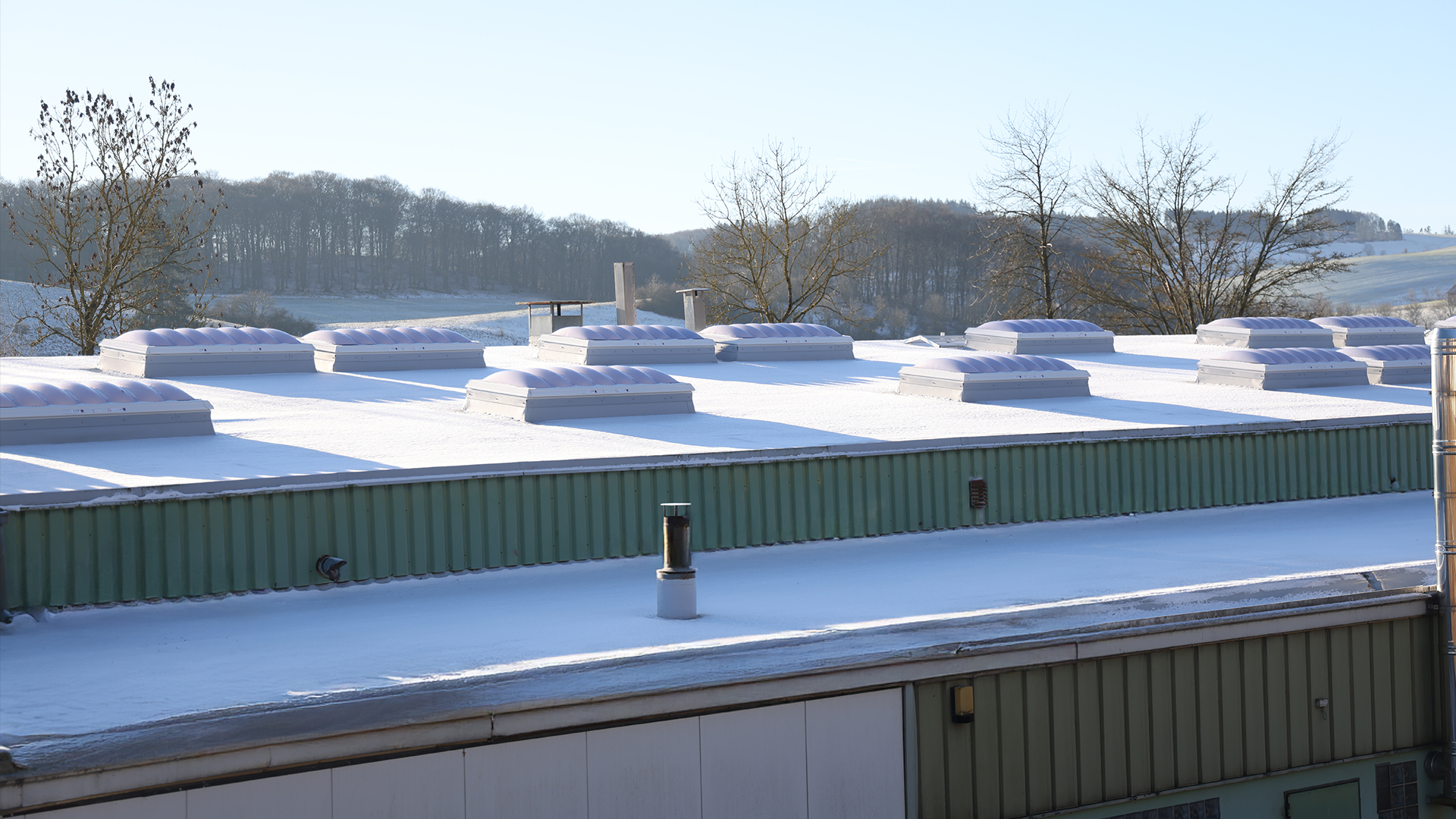 Snow-covered flat roof of the "Ab in die Box" building at Diemelsee with wave-shaped skylights.