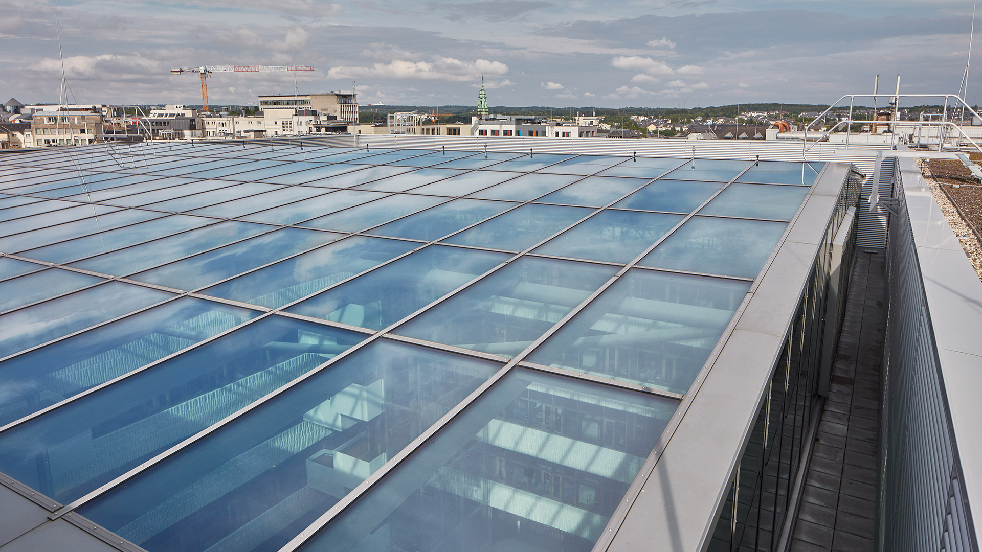 Glasdachkonstruktion des Postgebäudes in Luxemburg mit LAMILUX Glasdach PR60 Passivhaus-System, aufgenommen von außen mit Gebäuden im Hintergrund.