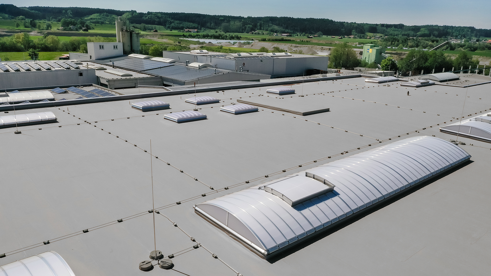 Aerial view of the production hall of the Unglehrt construction company with LAMILUX F100 W skylights, B light bands, and solar panels on the roof.